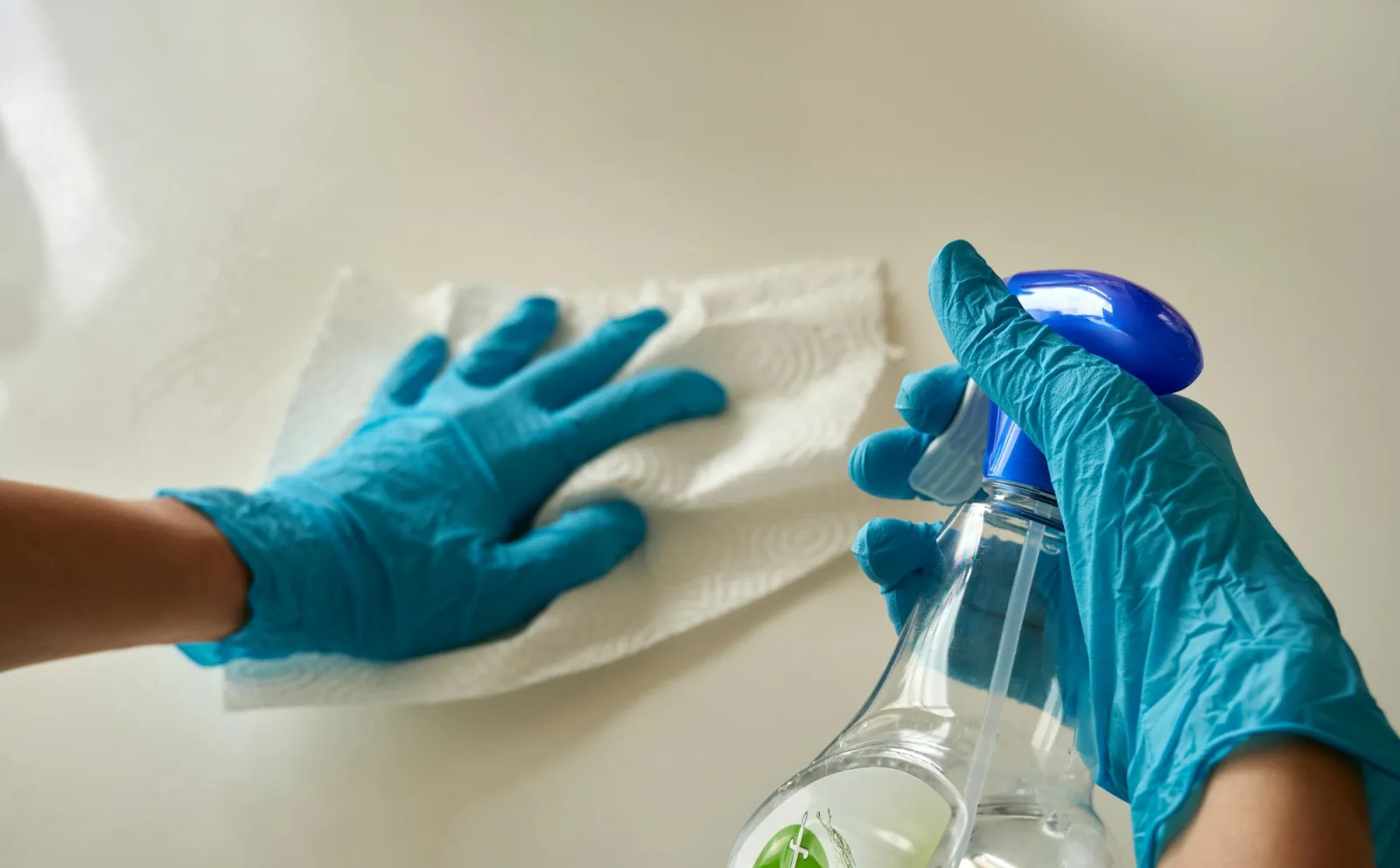 Gros plan de mains gantées essuyant une surface blanche, vaporisateur à la main