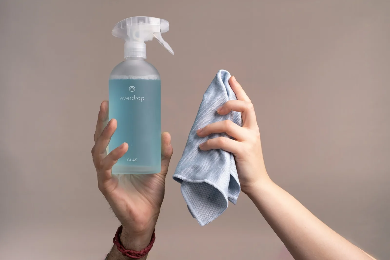 Deux mains tenant un vaporisateur rempli de liquide turquoise et un chiffon en microfibre