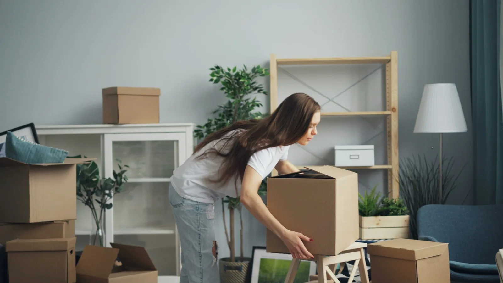 Personne soulevant une boîte de carton dans un salon clair encombré de cartons de déménagement